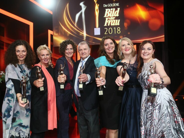 Sechs Preisträgerinnen in Abendkleidern und ein Mann der GOLDENEN BILD der FRAU-Gala 2018 halten ihre goldene Figurine in die Kamera 